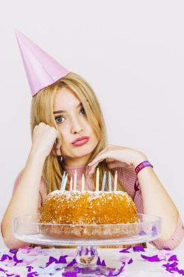 Gelangweilte Frau mit Partyhut und Geburtstagstorte