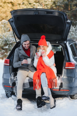 Paar beim Date im Winter sitzt mit Decke im Kofferraum und trinkt Heißgetränke