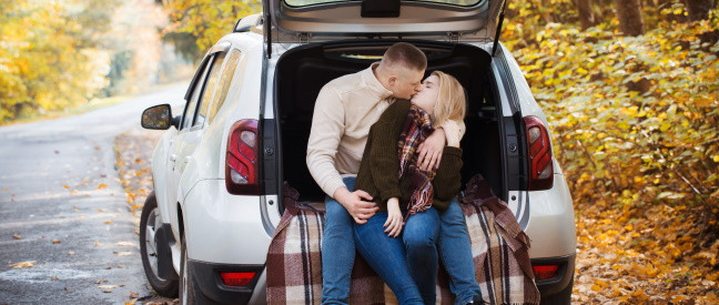 Paar sitzt beim Date im Kofferraum vom Auto und küsst sich