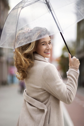 Lächelnde Frau mit Regenschirm blickt über die Schulter