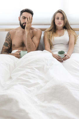 Unglückliches Paar sitzt nebeneinander mit Kaffeetassen im Bett