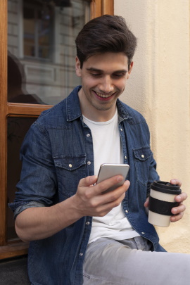 Mann draußen vorm Fenster schaut lächelnd aufs Handy