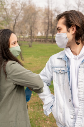 Maske tragendes Paar bei der Begrüßung im Park