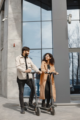 Mann und Frau auf E-Scootern vor Firmengebäude