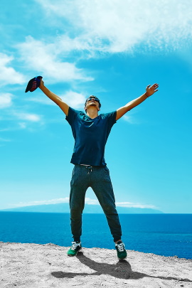 Mann steht glücklich jubelnd vor dem blauen Meer