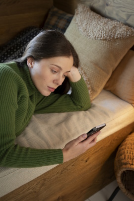 Frau liegt gelangweilt auf dem Bett und liest Nachricht am Handy