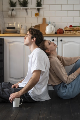 Paar sitzt mit Rücken zueinander auf dem Boden in der Küche