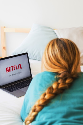 Frau schaut Netflix mit Laptop auf dem Bett