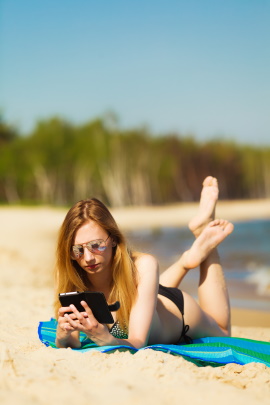 Frau liegt mit Handy am Strand und macht Online-Dating