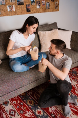Mann und Frau sitzen im Wohnzimmer und essen asiatische Nudeln aus der Box