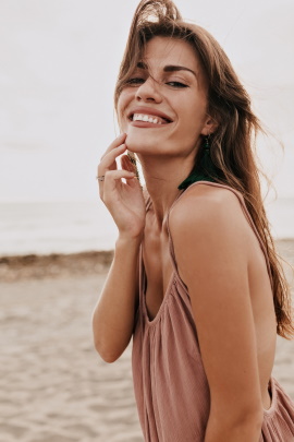Frau am Strand lächelt und fasst sich ans Kinn