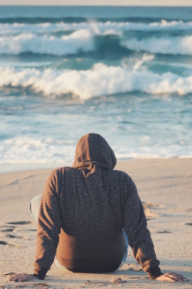 Person im Kapuzenpullover schaut auf Wellen im Meer