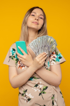 Lachende Frau mit Handy und gefächerten Geldscheinen