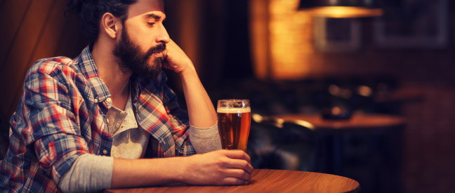 Mann sitzt traurig in Kneipe mit einem Glas Bier