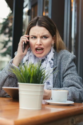 Frau sitzt im Café und spricht wütend ins Handy