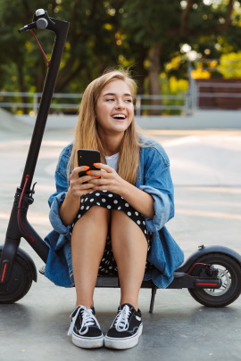 Frau mit Smartphone sitzt lachend auf einem E-Scooter