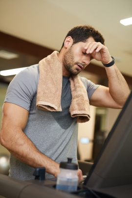 Verschwitzter Mann steht erschöpft im Fitnessstudio
