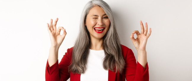 Ältere Frau zeigt lächelnd das Okay-Zeichen mit den Händen