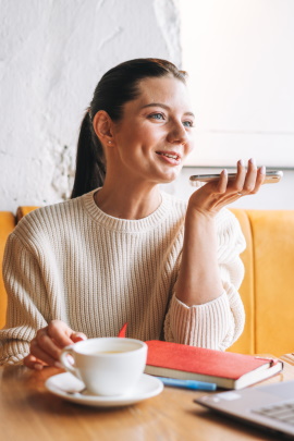Frau im Café nimmt Sprachnachricht am Smartphone auf
