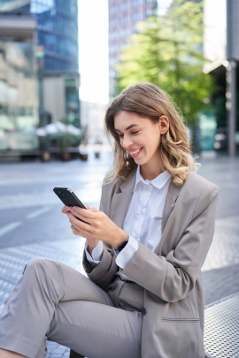 Frau in der Stadt schaut lächelnd aufs Handy