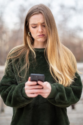 Frau im herbstlichen Park schaut kritisch aufs Handy