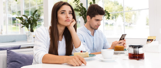 Frau gelangweilt von Mann, der beim Date im Café aufs Handy schaut
