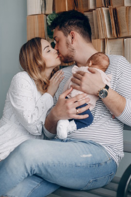 Mann küsst Partnerin und hält dabei Baby in den Armen