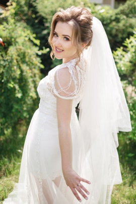 Lächelnde Frau im Hochzeitskleid steht im Garten