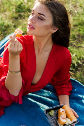 Erotische Frau auf Picknickdecke isst Sushi