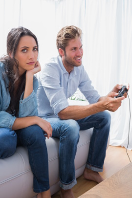 Frau sitzt gelangweilt neben Partner, der Videospiel spielt