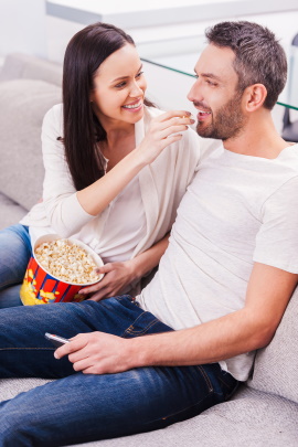 Frau füttert Mann mit Popcorn zu Hause auf dem Sofa