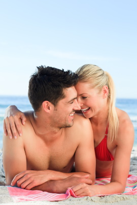 Paar am Strand sitzt glücklich zusammen auf dem Handtuch