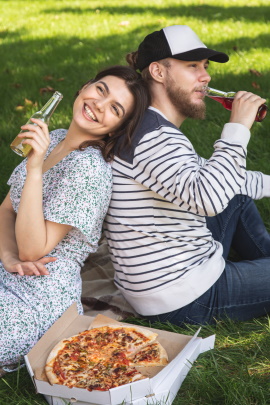 Paar sitzt mit Pizza und Drinks auf der Wiese