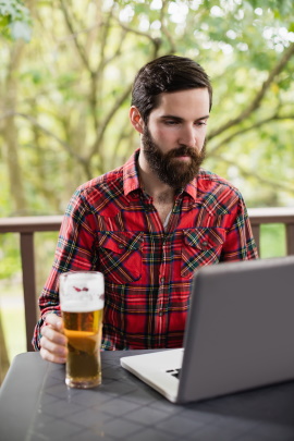 Bärtiger Mann sitzt draußen am Laptop mit Glas Bier