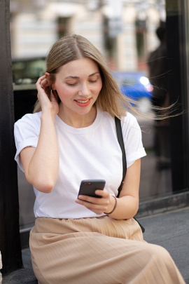 Sitzende Frau schaut lächelnd aufs Smartphone
