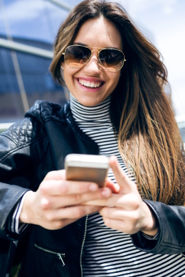Frau in der Stadt schaut lachend aufs Handy