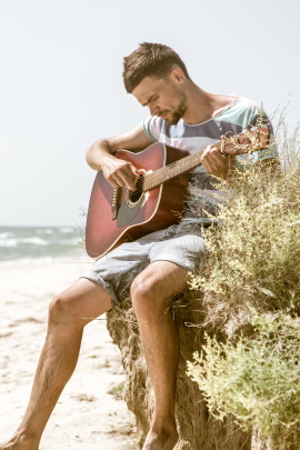 Foto von Mann, der am Strand Gitarre spielt