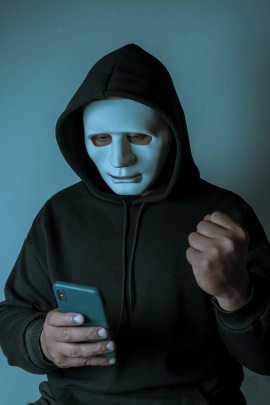 Mann mit Maske schaut im Dunkeln aufs Handy