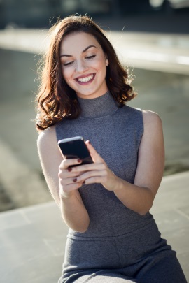 Lachende Frau sitzt draußen und liest Nachricht am Handy