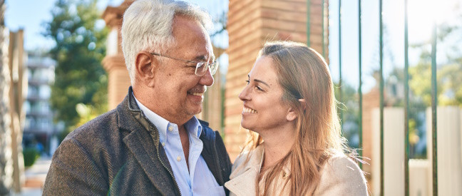 Älterer Mann und jüngere Frau lächeln sich verliebt an