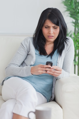 Frau sitzt auf dem Sofa und schaut verärgert aufs Handy
