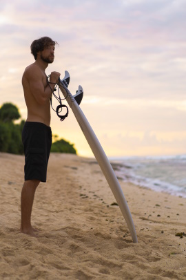 Mann steht mit Surfbrett am Strand