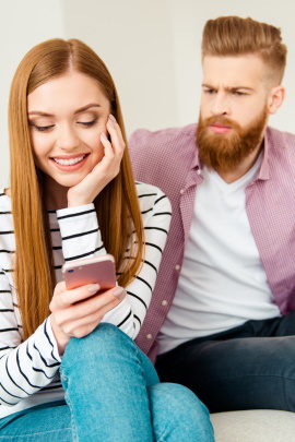 Mann schaut eifersüchtig der Frau beim Lesen im Handy zu