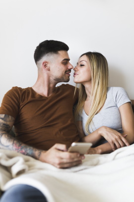 Paar mit Smartphone küsst sich verliebt im Bett