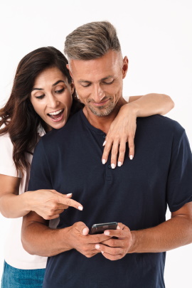 Frau schaut Mann mit Handy lachend über die Schulter
