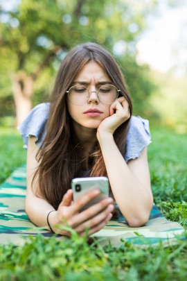 Frau liegt auf der Wiese und schaut kritisch aufs Smartphone